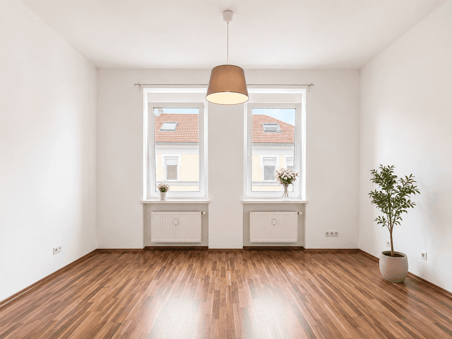 Heller, leerer Raum mit zwei großen Fenstern, Holzboden und weiß gestrichenen Wänden.