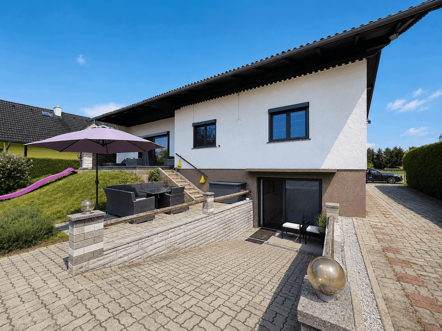 Außenansicht des Hauses mit gepflasterter Zufahrt und Terrasse.