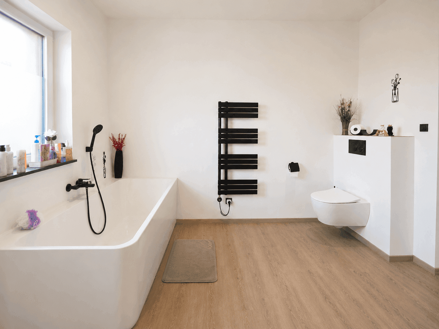 Helles Badezimmer mit Badewanne, wandhängendem WC und modernem Handtuchheizkörper.