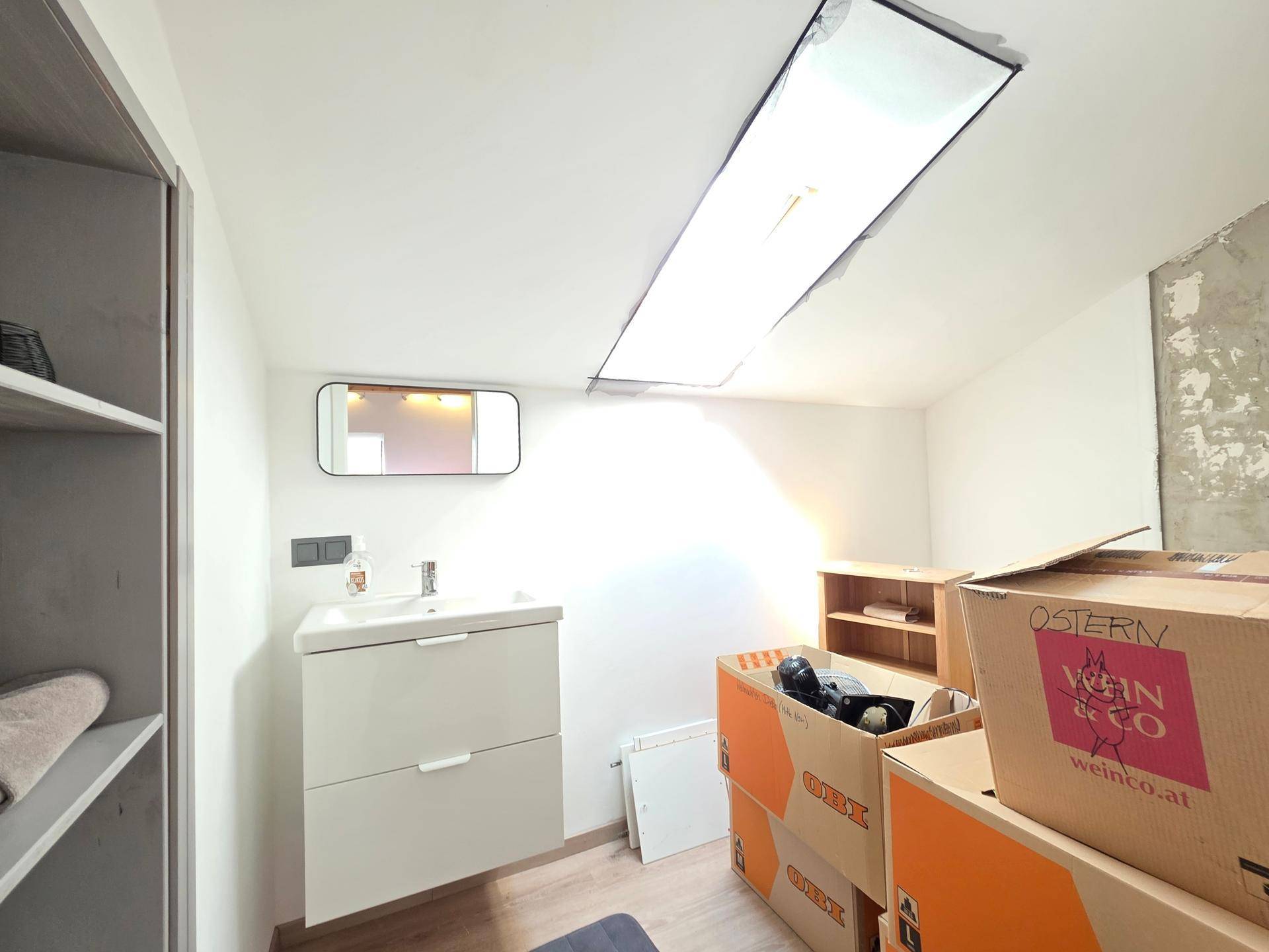 Badezimmer im Dachgeschoss mit Waschtisch, Spiegel und Dachfenster.