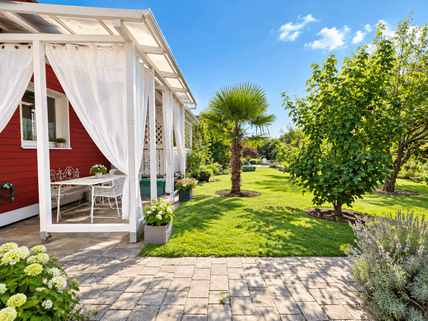Rotes Haus mit überdachter Terrasse und weitläufigem, sonnigem Garten mit Palme.