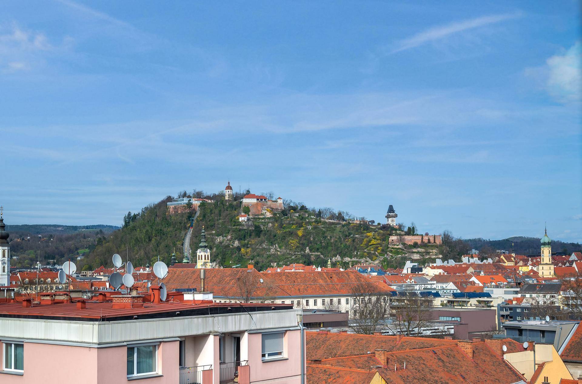 Panoramablick auf die Stadt mit historischer Burg auf einem Hügel unter blauem Himmel.