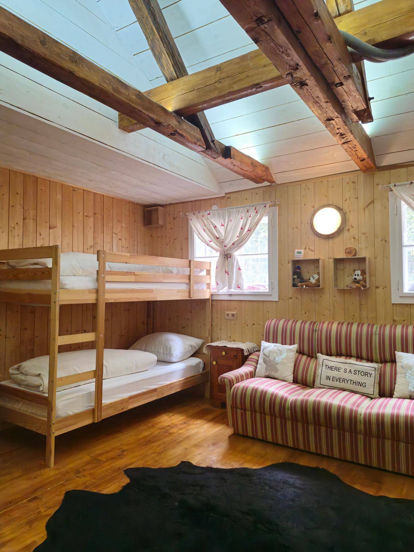 Gemütliches Schlafzimmer mit Etagenbett, Holzvertäfelung und sichtbaren Holzbalken unter der Decke.