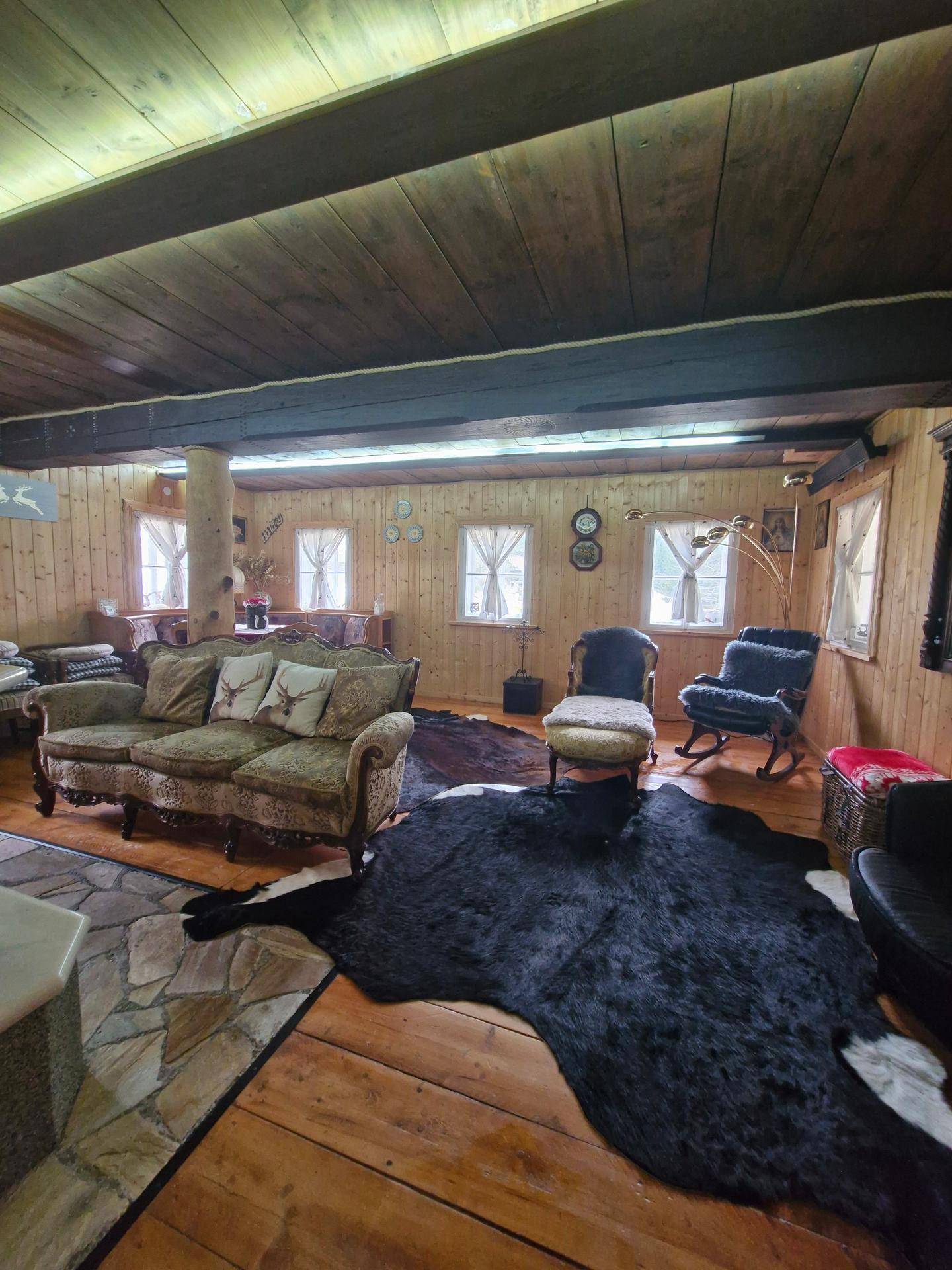 Geräumiges Wohnzimmer mit Holzboden, rustikalen Möbeln und dunklen Deckenbalken.