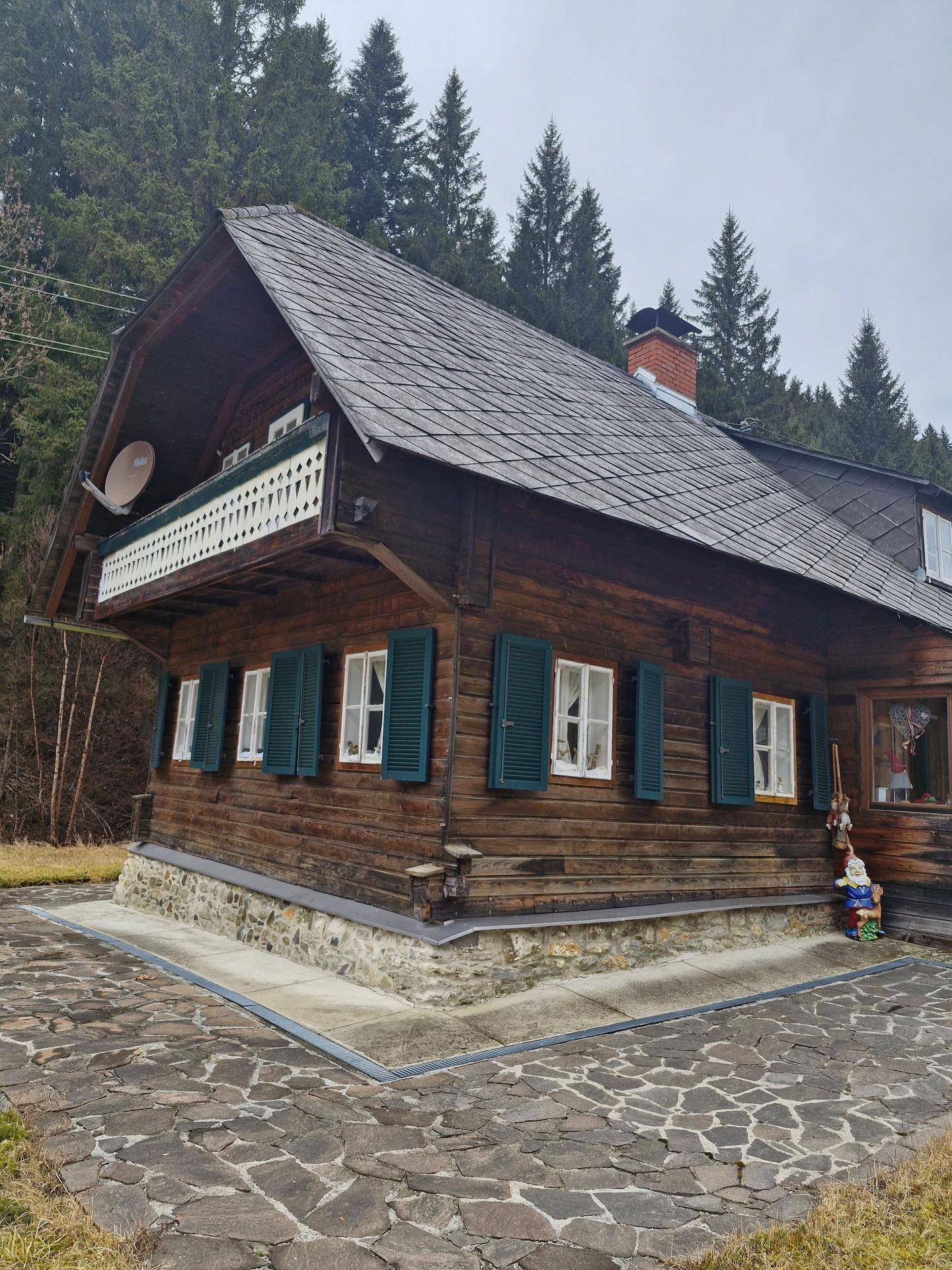 Traditionelles Holzhaus mit Balkon, grünen Fensterläden und Schindeldach in alpiner Landschaft.
