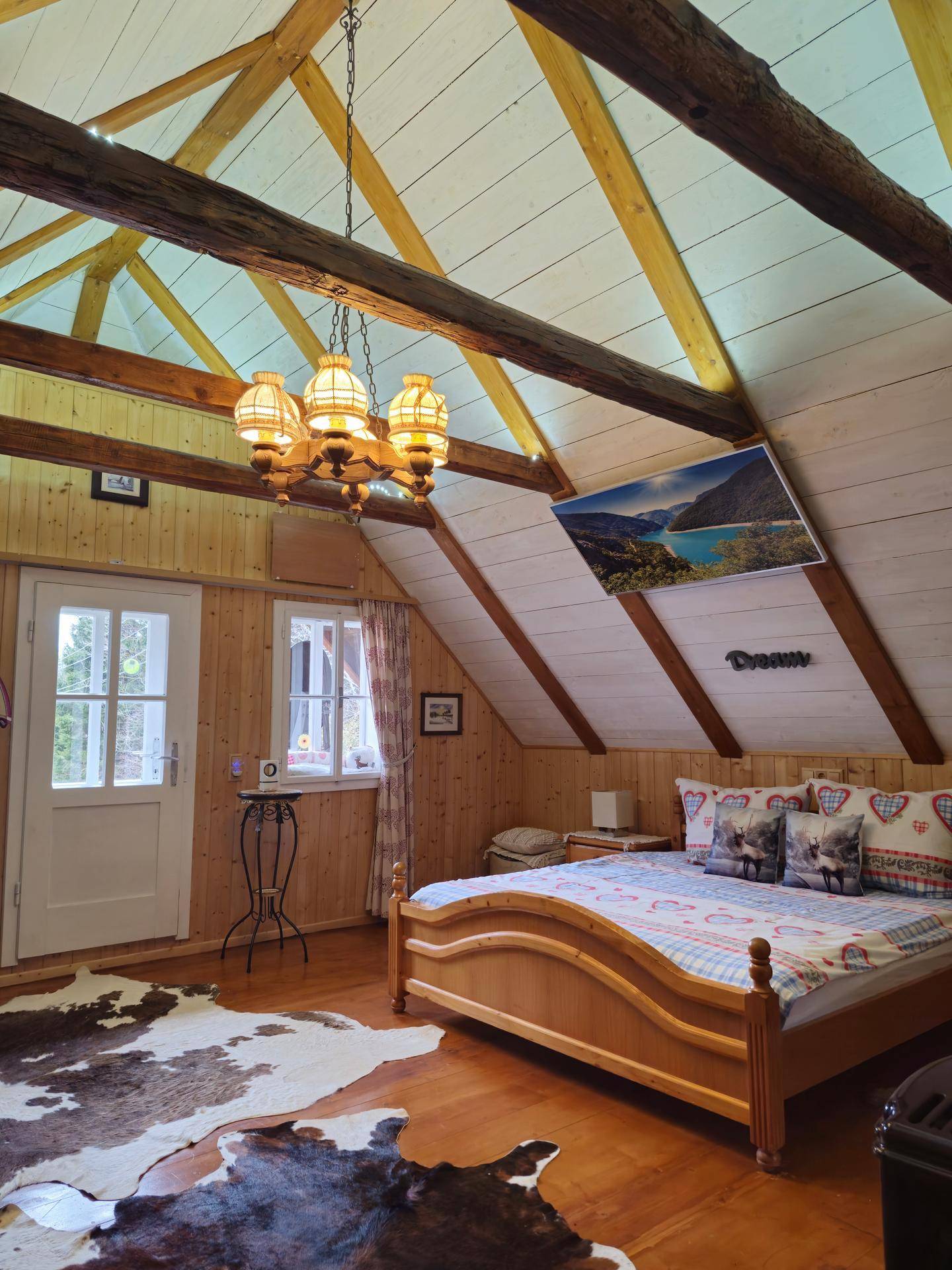 Rustikales Schlafzimmer mit Doppelbett, Holzbalken und schrägen Decken im Dachgeschoss.