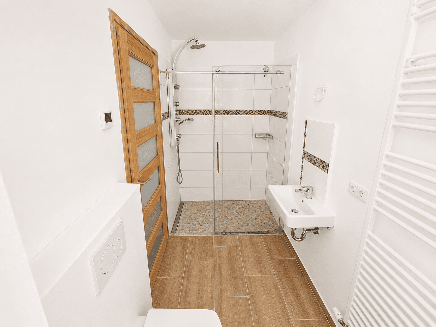 Modernes Duschbad mit ebenerdiger Dusche, wandhängendem WC, Einzelwaschbecken und Handtuchheizkörper.