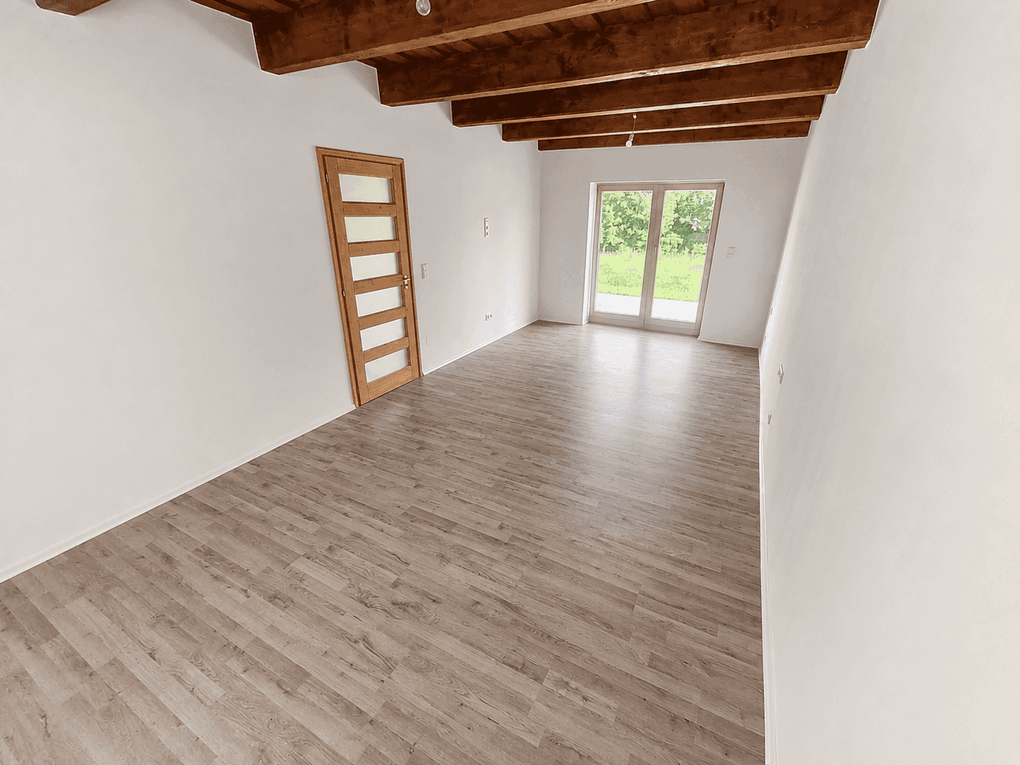 Heller Wohnraum mit Holzbalkendecke, Laminatboden und Zugang zum Garten oder zur Terrasse.