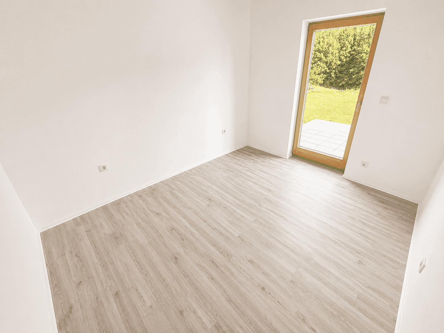 Geräumiges Zimmer mit Laminatboden und Tür zum Garten oder zur Terrasse.