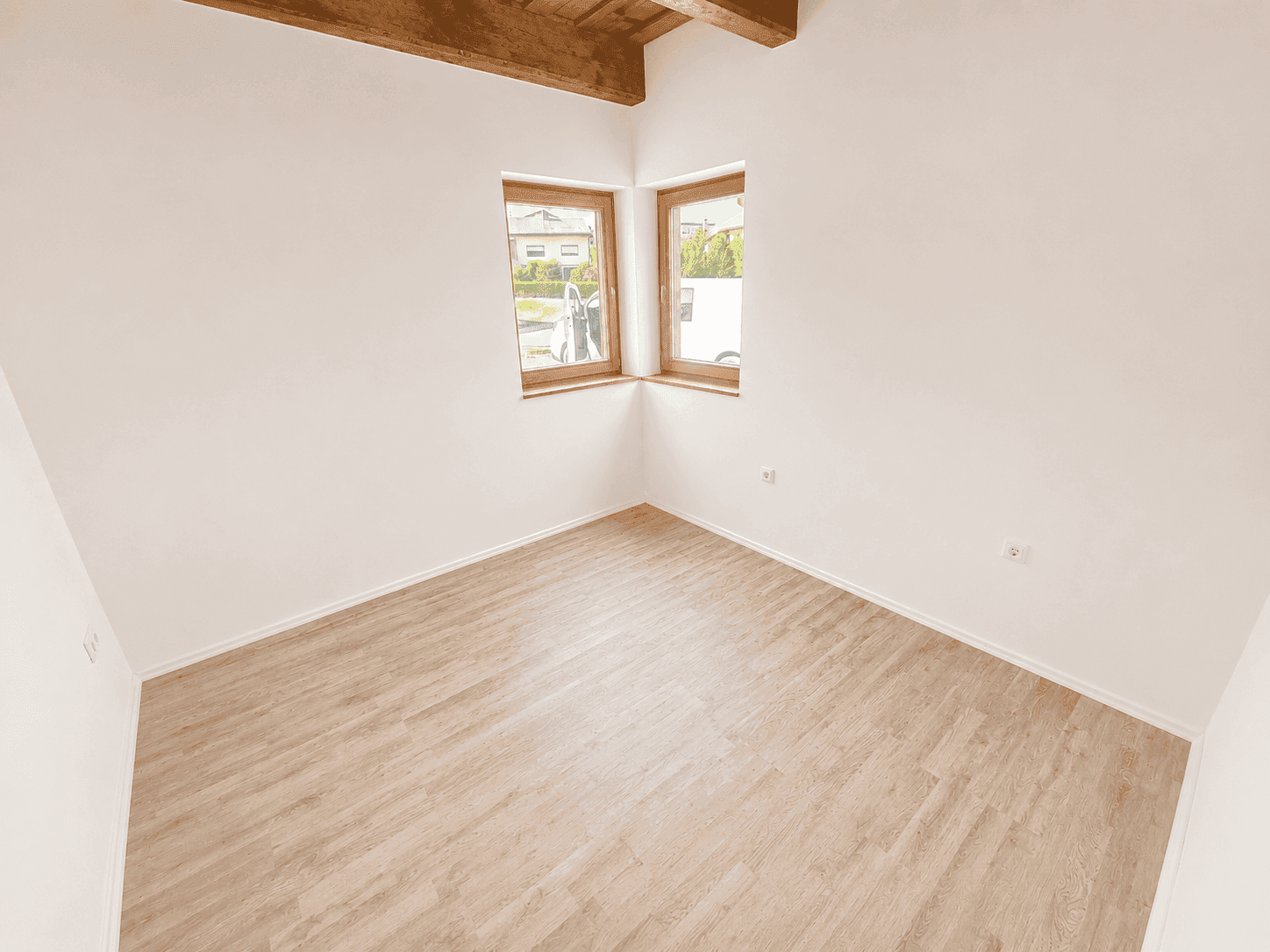 Helles Schlafzimmer mit Laminatboden, Holzbalken und zwei Fenstern für viel Tageslicht.