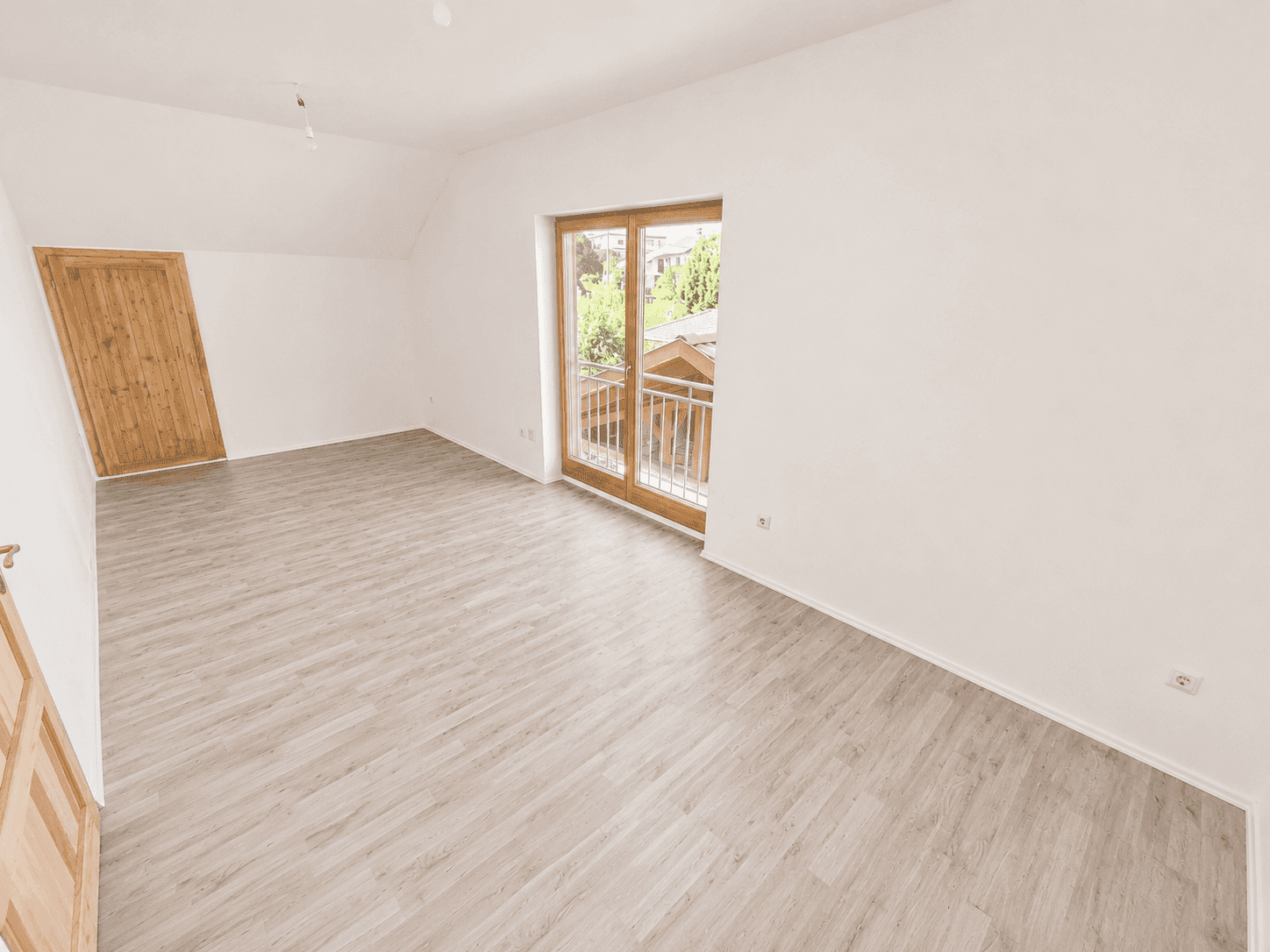 Helles Dachzimmer mit Laminatboden und französischem Balkon mit Blick ins Grüne.
