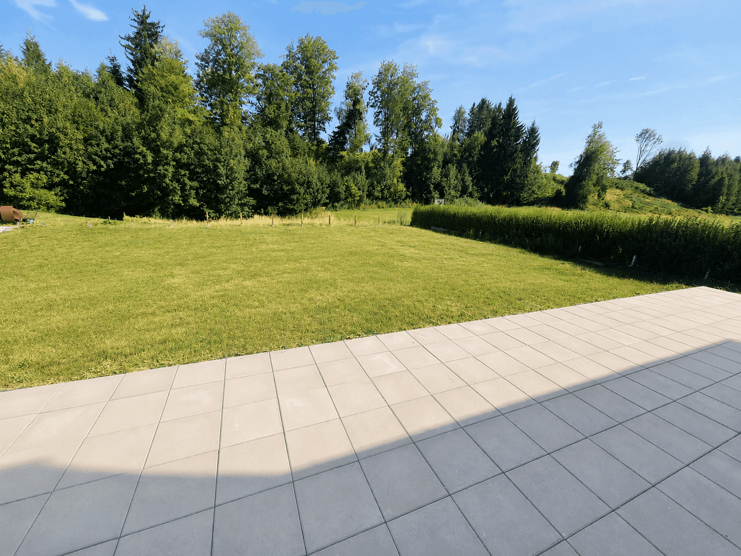 Großer, gepflegter Garten mit Rasenfläche und angrenzender Terrasse, umgeben von Bäumen und Hecken.