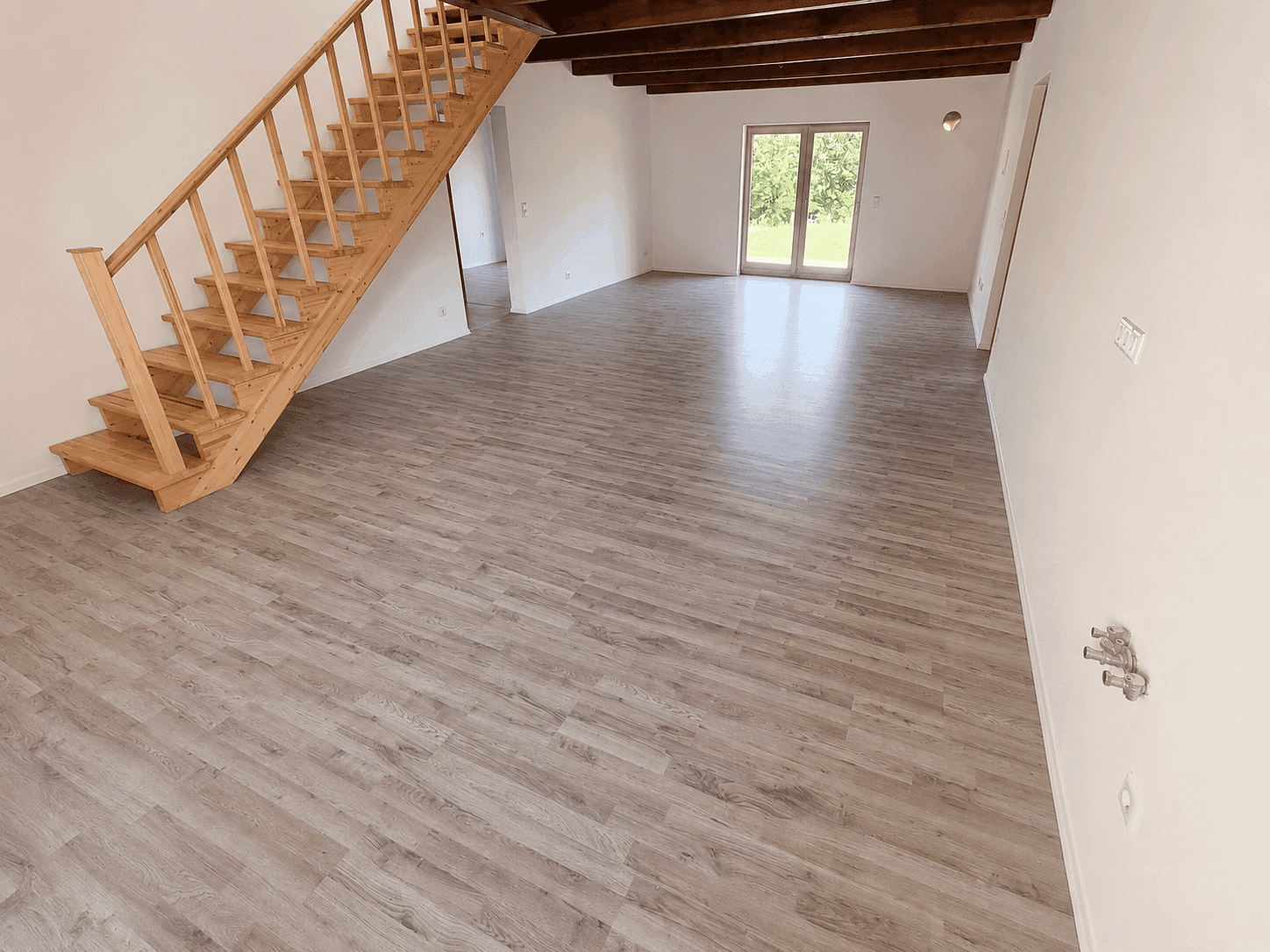 Geräumiger Wohnbereich mit Holztreppe, Laminatboden und Blick ins Grüne durch große Fenster.