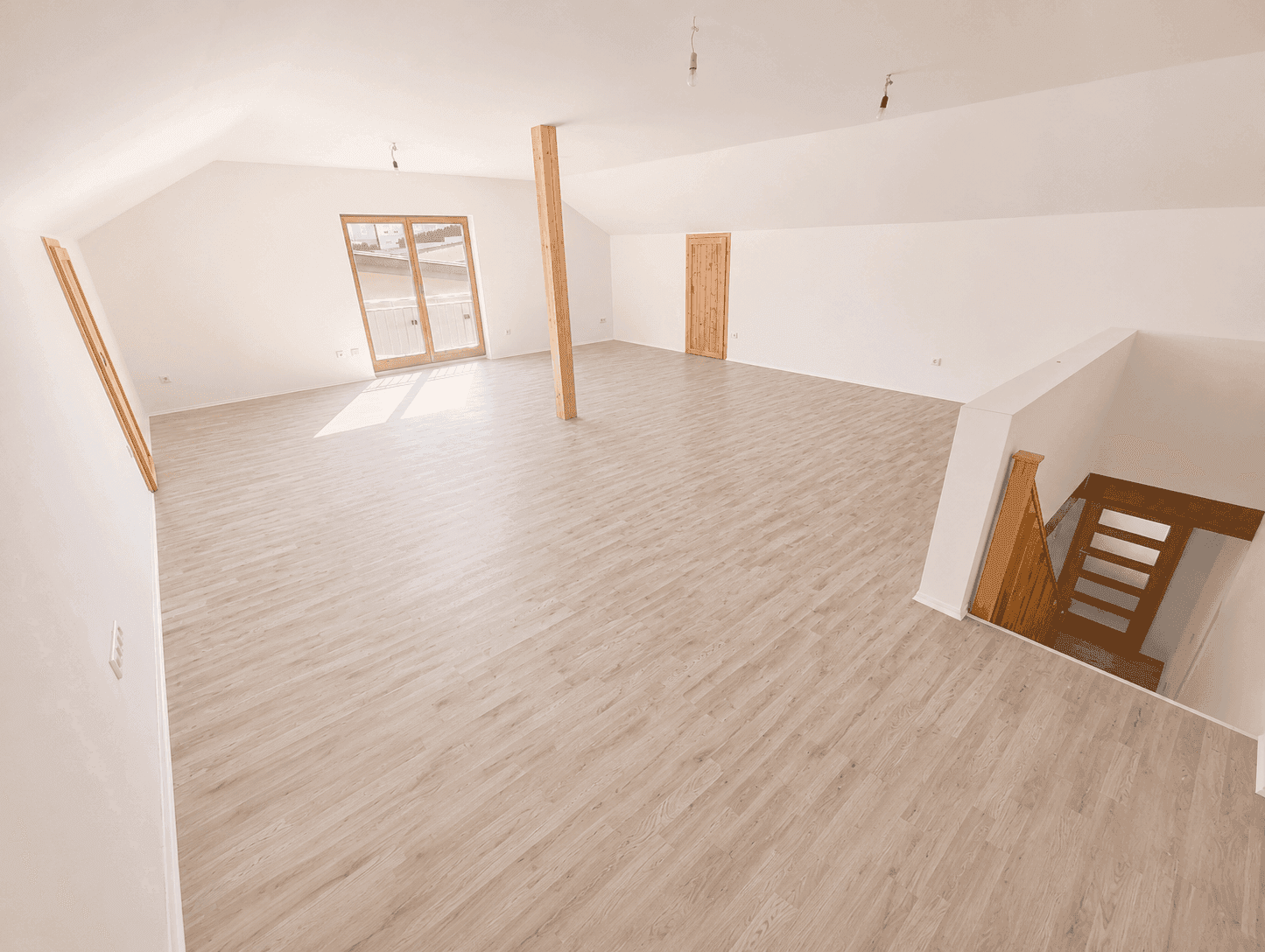 Ausgebauter Dachboden mit Laminatboden, Holzbalken und Zugang zu einem französischen Balkon.
