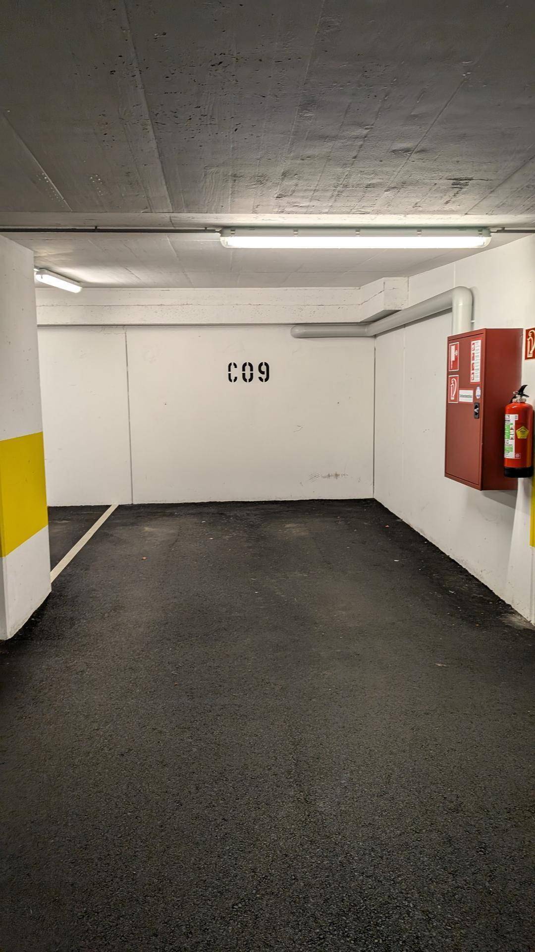 Leerer Tiefgaragenstellplatz mit klaren Bodenmarkierungen und einem Feuerlöscher an der Wand.