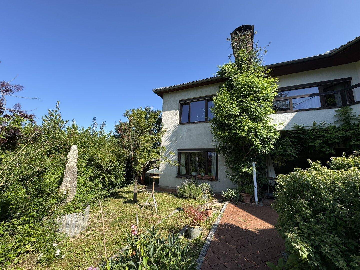 Seitenansicht des Hauses mit Gartenbereich und üppiger Vegetation unter blauem Himmel.