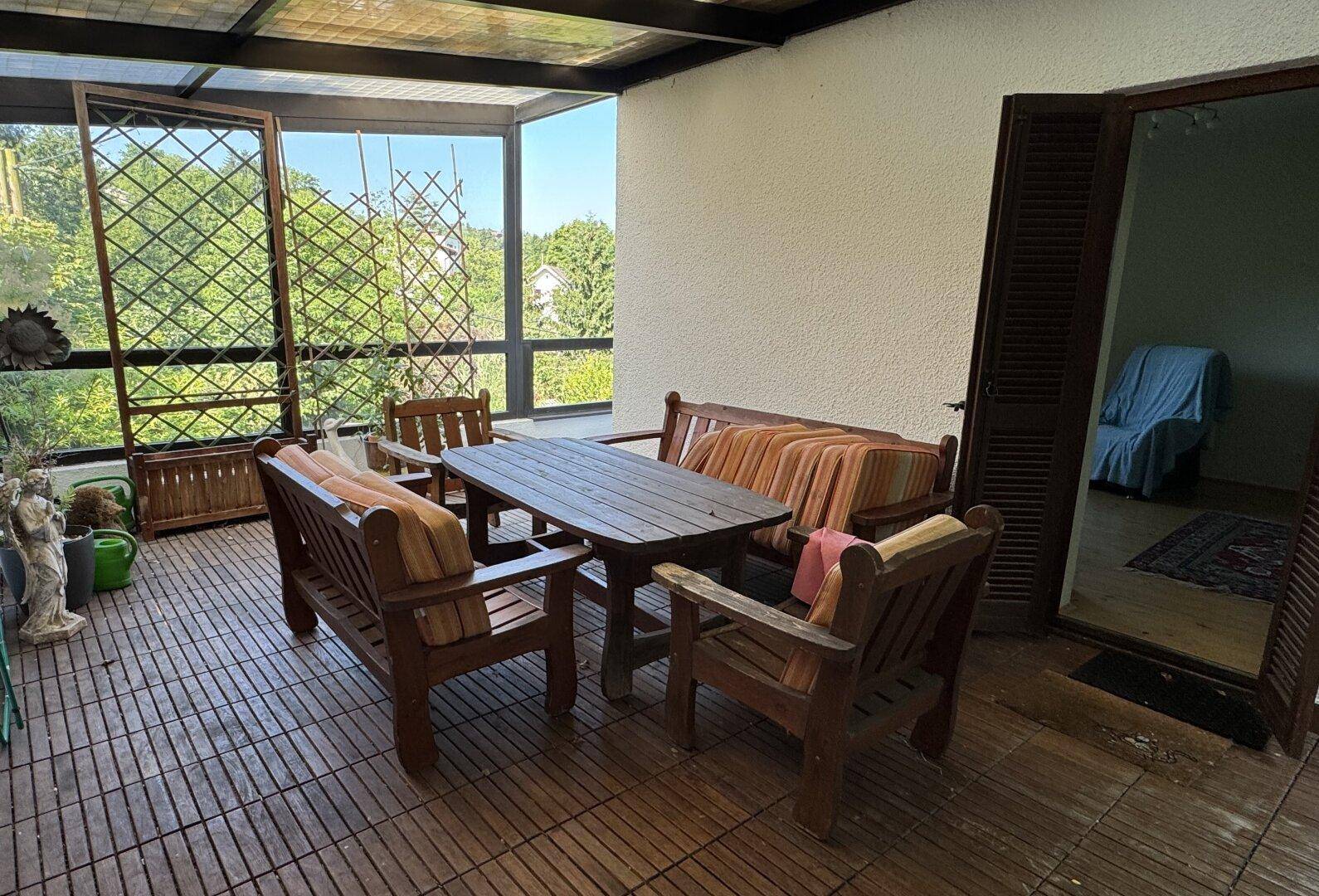 Überdachte Loggia mit Holzboden und Gartenmöbeln, ideal für entspannte Stunden im Freien.