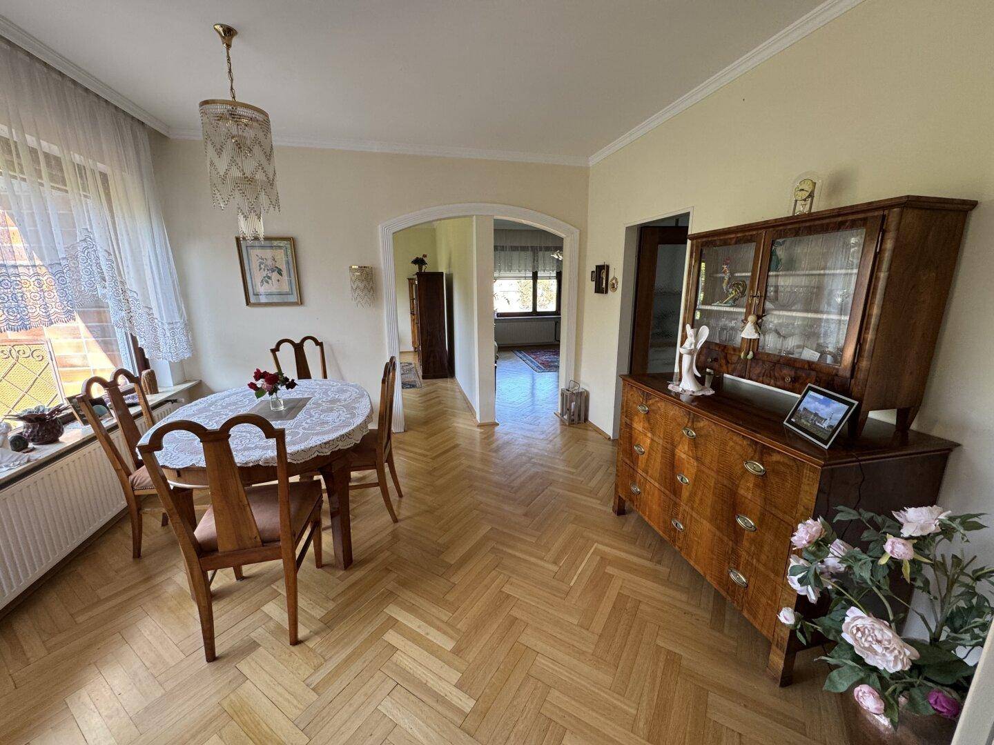 Helles Esszimmer mit Parkettboden, traditionellen Möbeln und Blick ins Grüne.