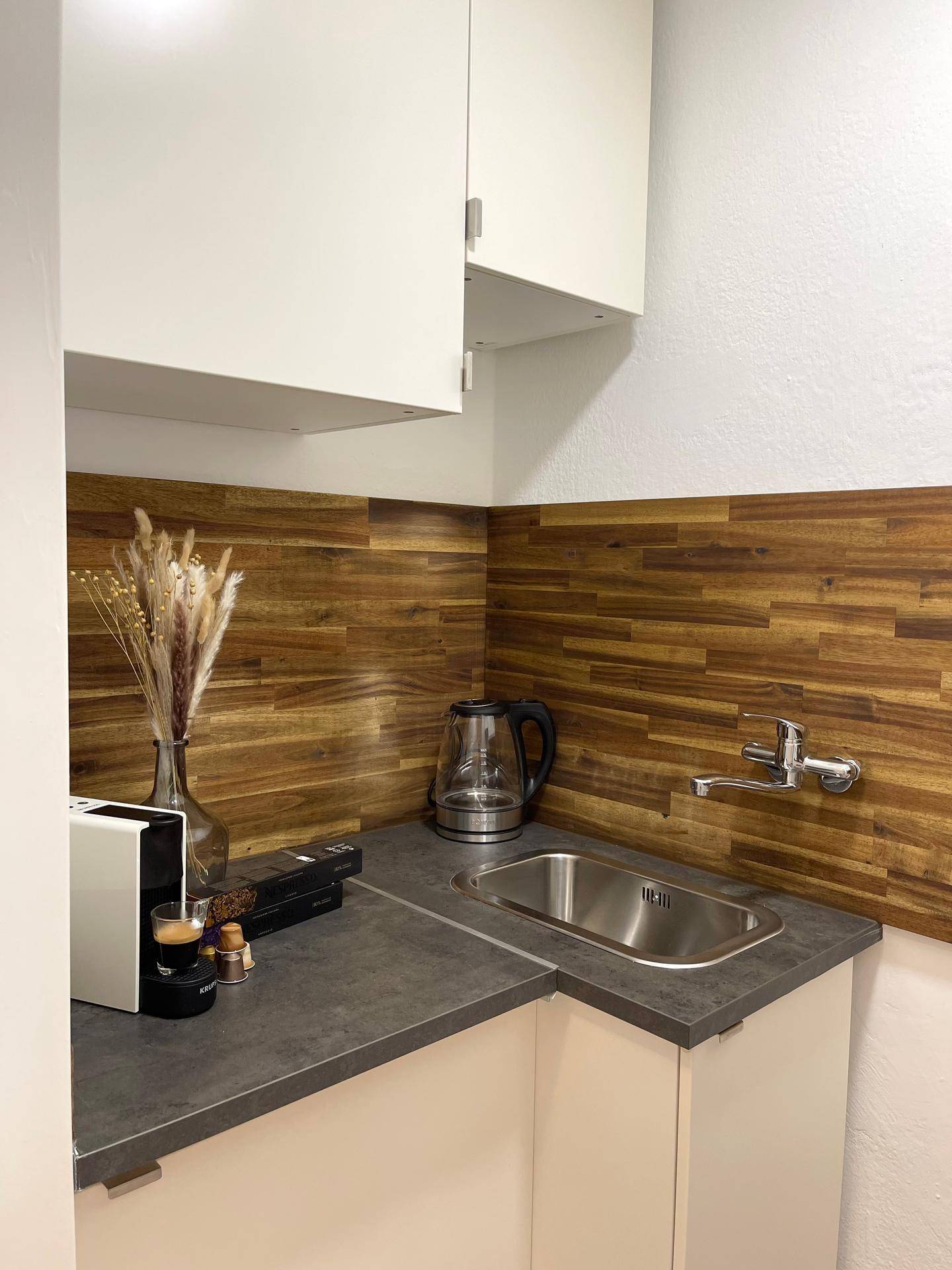 Funktionale Küchenzeile mit Spüle, Kaffeemaschine und einer stilvollen Holzrückwand.