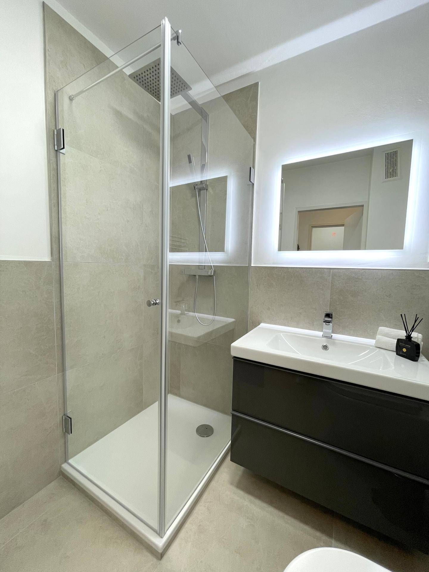 Modernes Badezimmer mit einer geräumigen Duschkabine, Waschtisch und beleuchtetem Spiegel.