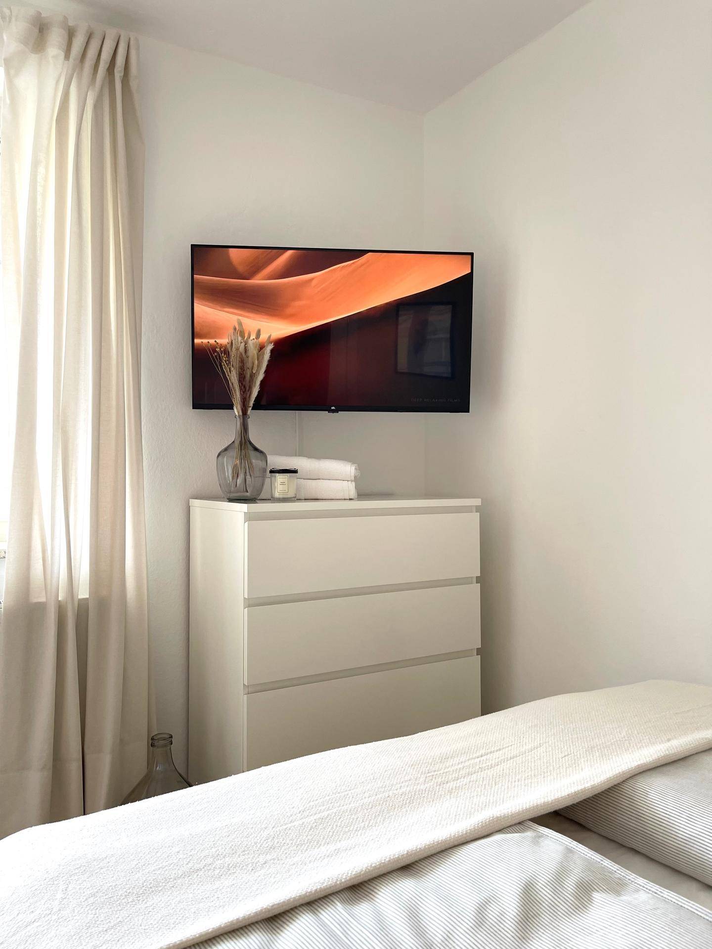 Detailansicht im Schlafzimmer mit einem an der Wand montierten Fernseher über einer weißen Kommode.