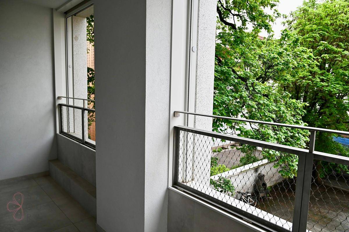 Schmaler Balkon mit modernen Metallgeländern und Blick auf grüne Bäume und die Straße.