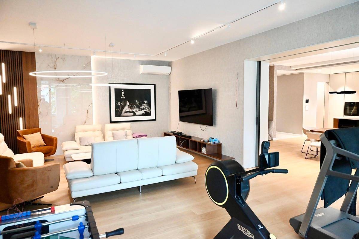 Großzügiges Wohnzimmer mit bequemen Sofas, Fernseher und Fitnessgeräten im Vordergrund.