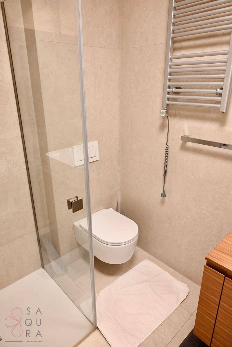 Modernes Badezimmer mit beigen Fliesen, wandhängendem WC, begehbarer Dusche und Handtuchheizkörper.