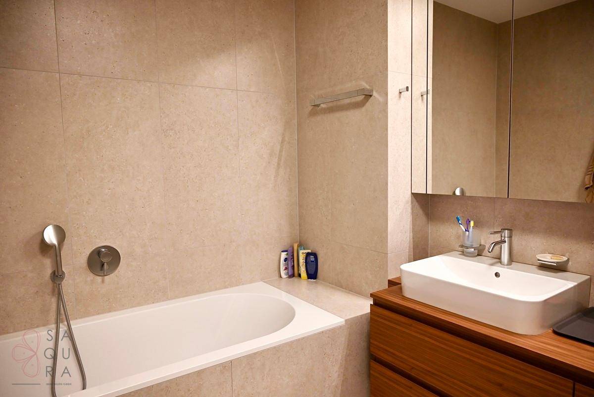 Modernes Badezimmer mit eingebauter Badewanne, beigen Fliesen und elegantem Holzwaschtisch.