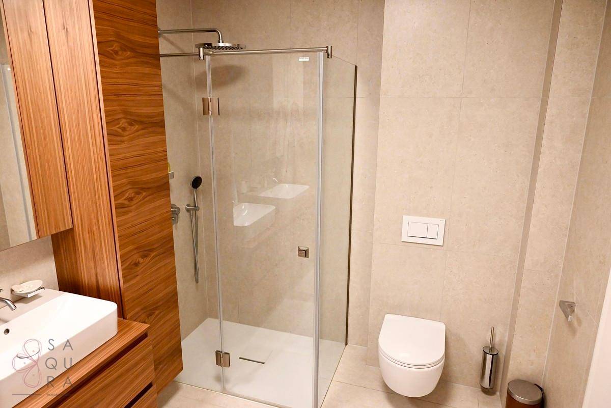 Helles Badezimmer mit beigen Fliesen, begehbarer Regendusche, wandhängendem WC und Holzwaschtisch.