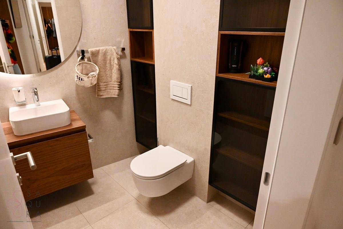 Modernes Gäste-WC mit elegantem Waschtisch, rundem Spiegel und integrierten Ablagefächern.