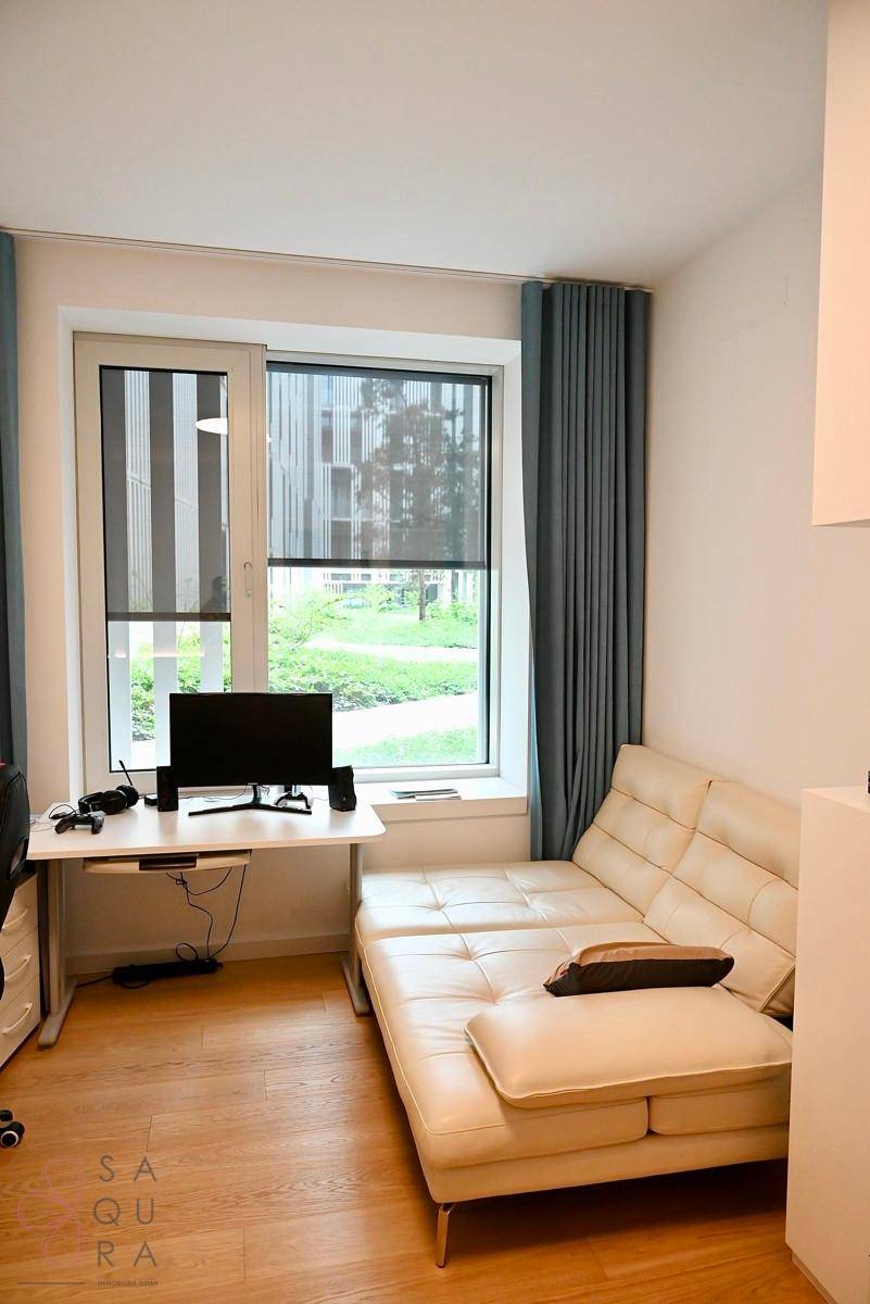 Helles Schlafzimmer mit Schreibtisch, Sofa und großem Fenster mit Blick ins Grüne.