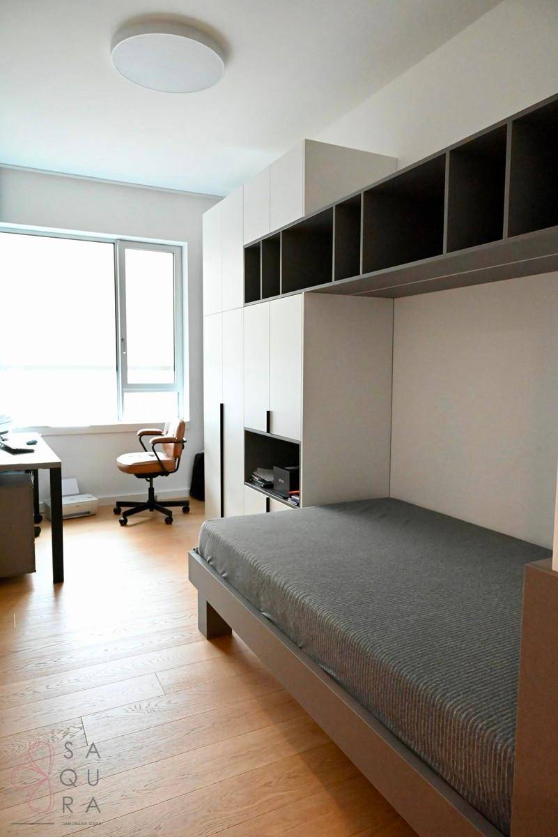 Helles Kinder- oder Gästezimmer mit Einzelbett, integrierten Regalen und einem Schreibtisch am Fenster.