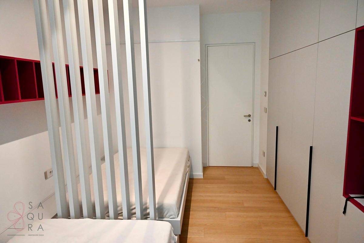 Modernes Schlafzimmer mit zwei Betten, Raumteiler und integrierten Kleiderschränken.