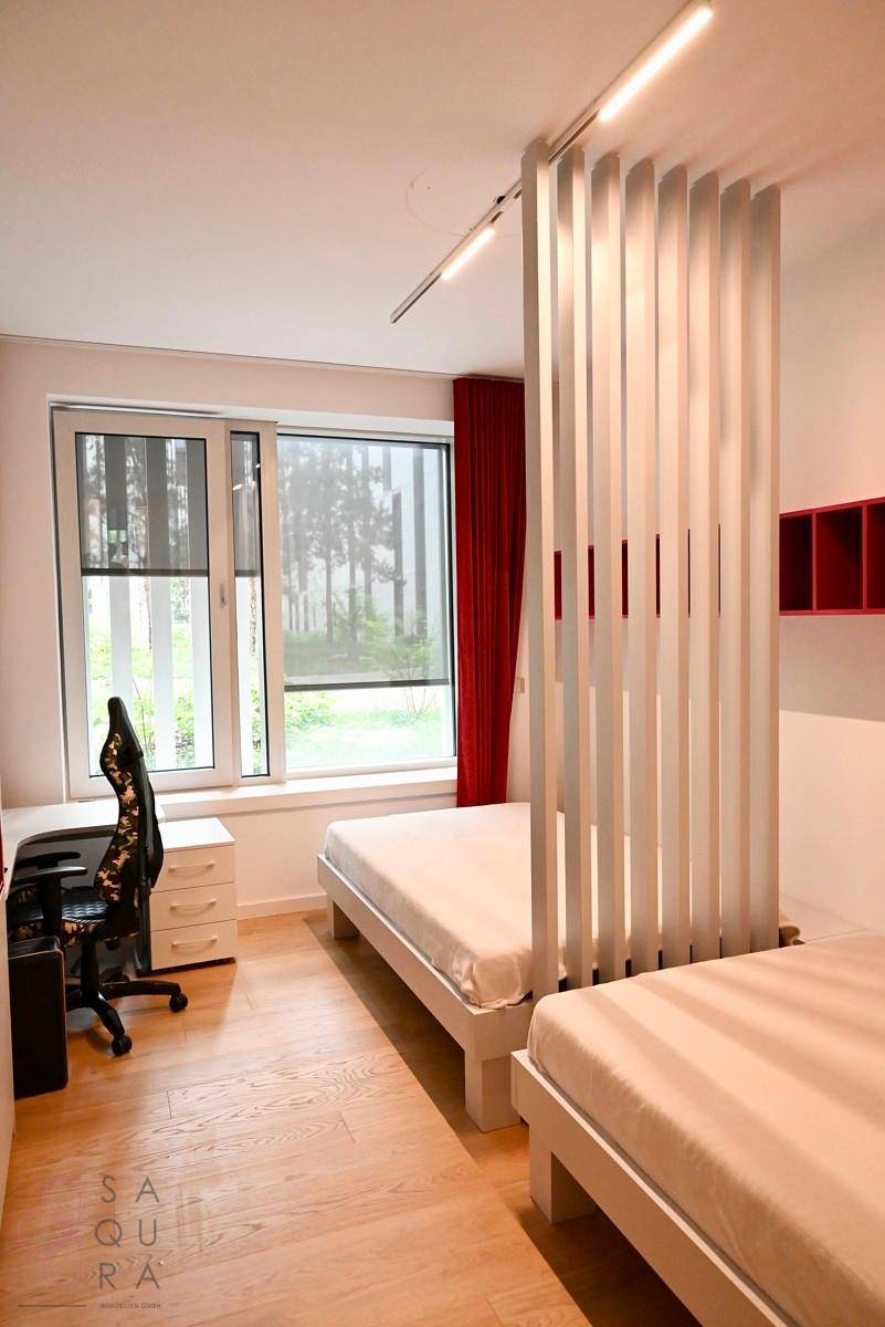 Helles Schlafzimmer mit zwei Einzelbetten, Schreibtisch und großen Fenstern mit rotem Vorhang.