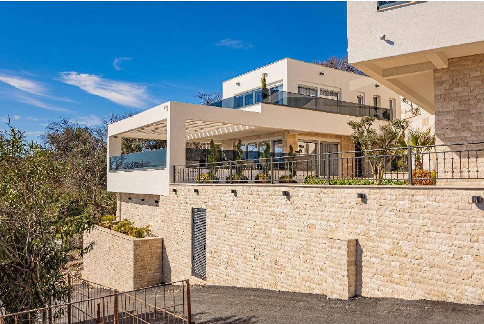 Ansicht der modernen Villa mit Steinfassade und Terrassenbereichen, eingebettet in die natürliche Umgebung.