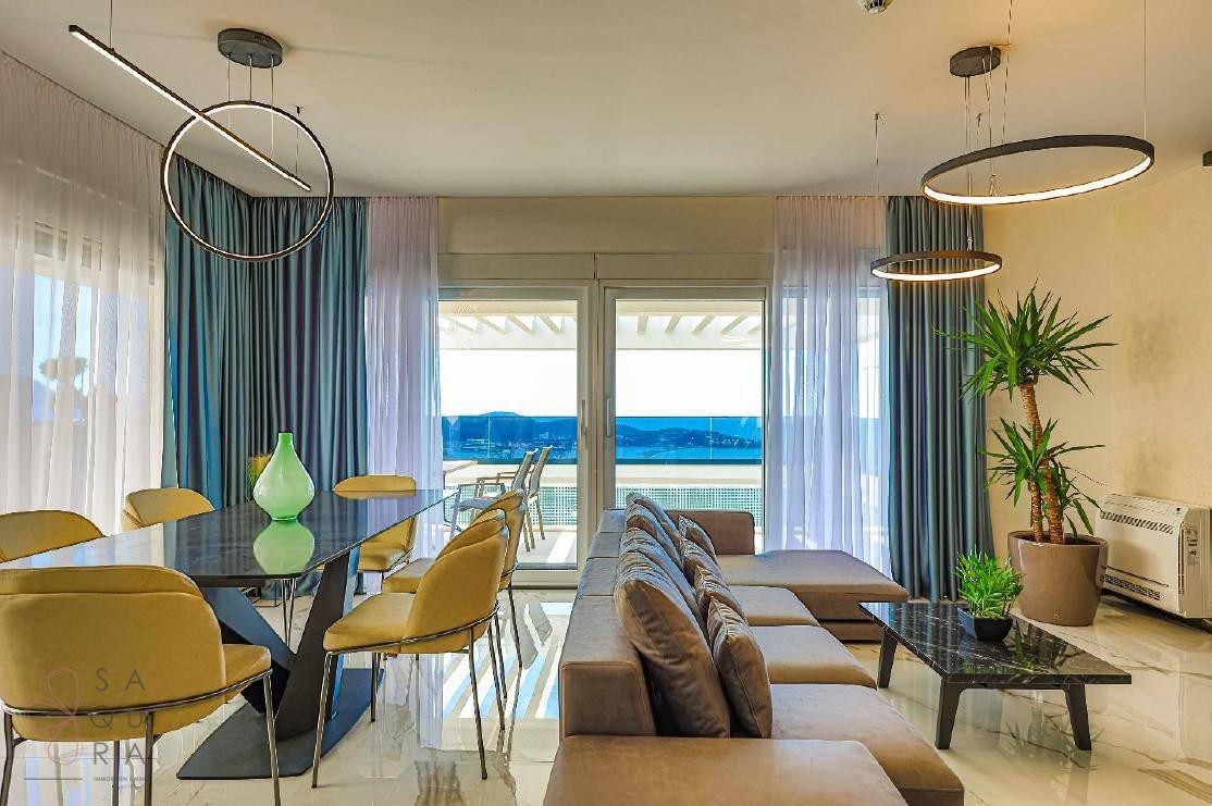 Heller Wohn- und Essbereich mit modernen Möbeln, stilvollen Leuchten und Zugang zur Terrasse mit Meerblick.