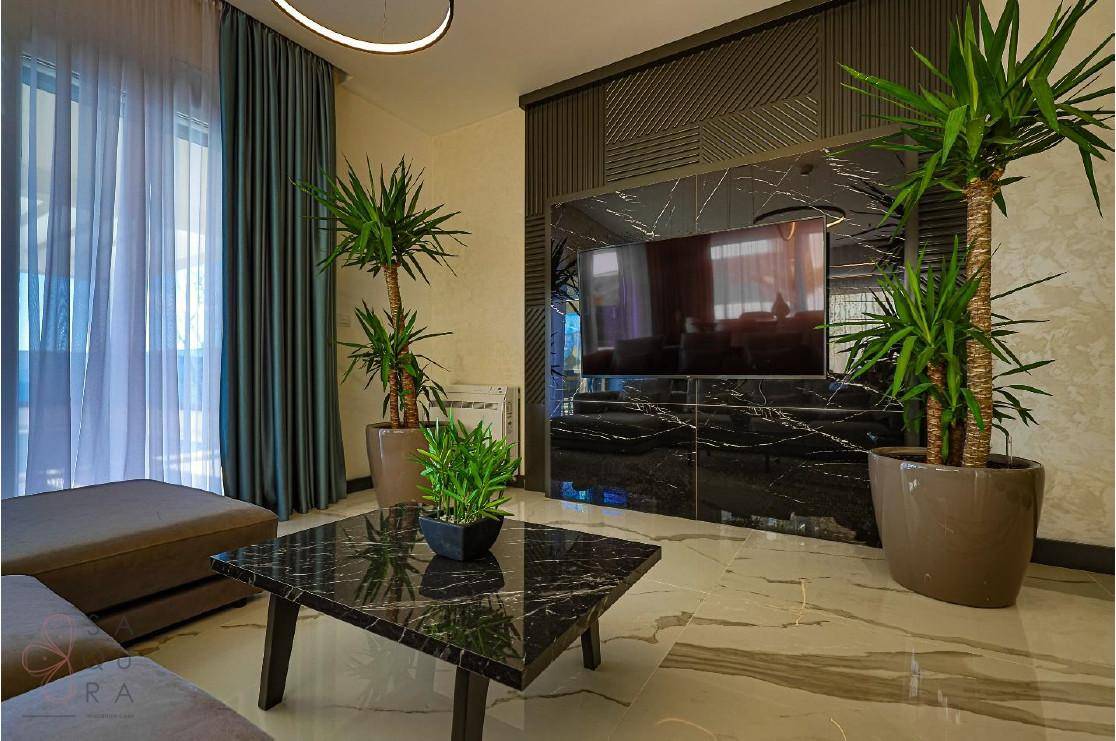 Modernes Wohnzimmer mit großem Fernseher, stilvollem Couchtisch und dekorativen Pflanzen.