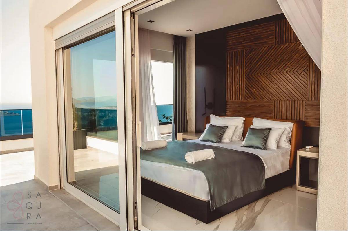 Helles Schlafzimmer mit Doppelbett, Holzwandverkleidung und Schiebetüren zur Terrasse mit Meerblick.