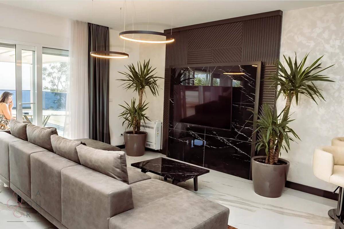 Elegantes Wohnzimmer mit beiger Eckcouch, dunklem Medienelement und Blick auf die Terrasse.