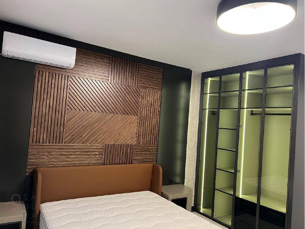 Schlafzimmer mit dekorativer Holzwand, offenem beleuchtetem Kleiderschrank und Klimaanlage.