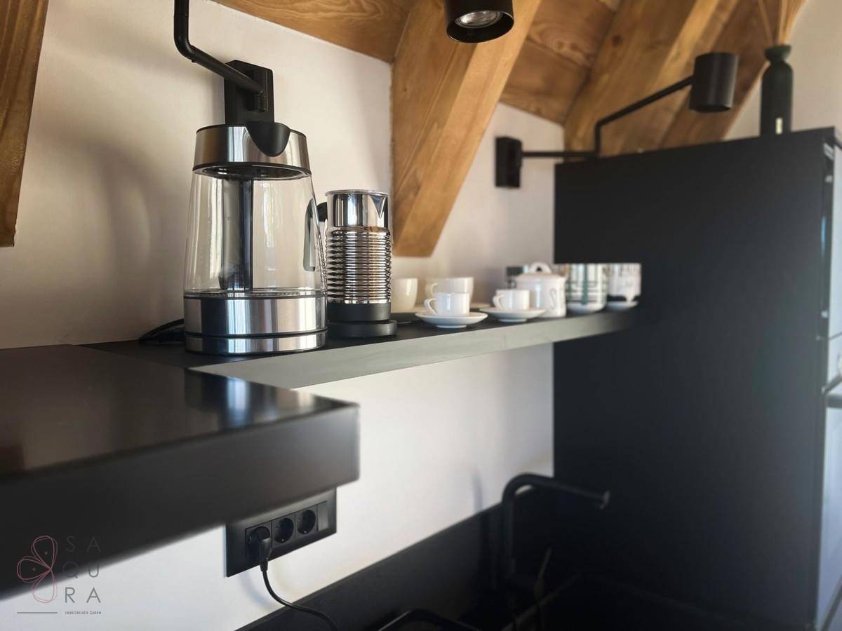 Moderne Küchenzeile mit Wasserkocher, Kaffeemaschine und Geschirr auf offenen Regalen.