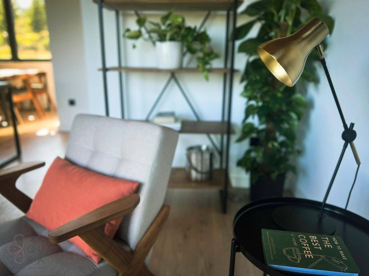 Detailansicht einer Leseecke mit modernem Sessel, Beistelltisch und goldener Lampe.