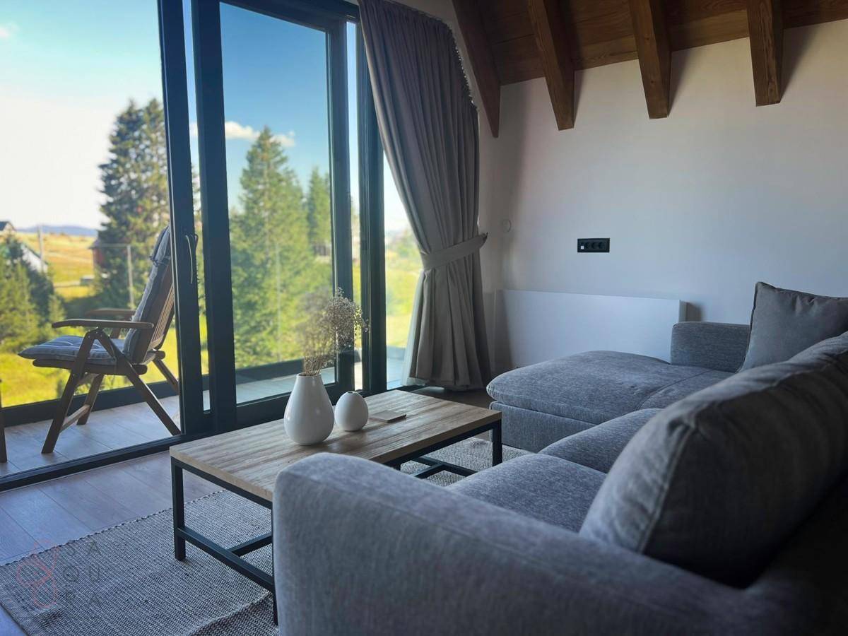 Modernes Wohnzimmer mit bequemer Couch, Holztisch und großen Fenstern zur Natur.