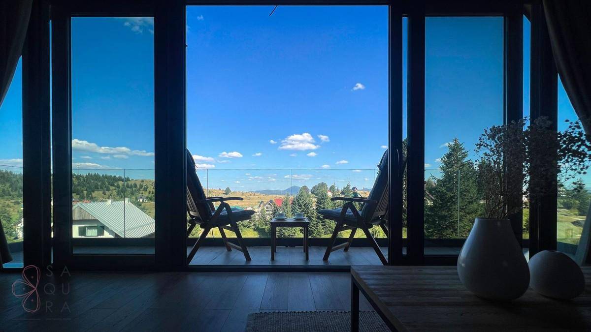Heller Wohnbereich mit großen Fenstern und Zugang zu einem Balkon mit Panoramablick.