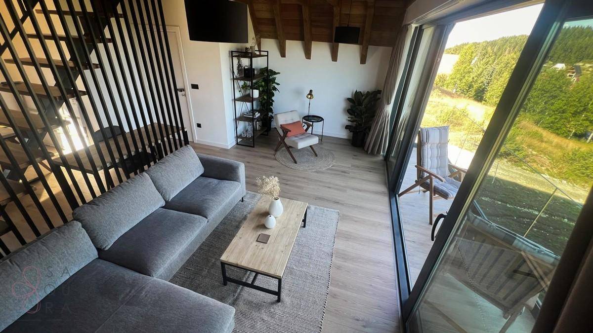 Heller Wohnbereich mit gemütlicher Sitzecke, Holzboden und Zugang zum Balkon.