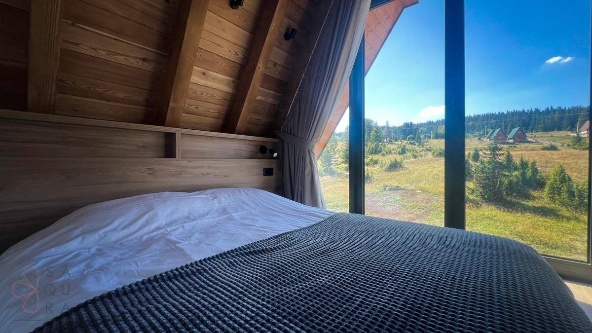 Gemütliches Schlafzimmer mit Holzwänden, großem Bett und Panoramablick durch bodentiefe Fenster.