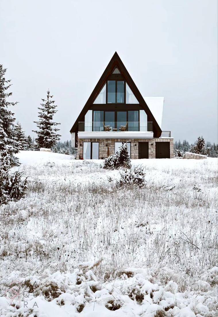 Modernes A-Rahmen-Haus in einer verschneiten Landschaft mit großen Fenstern und Balkon.