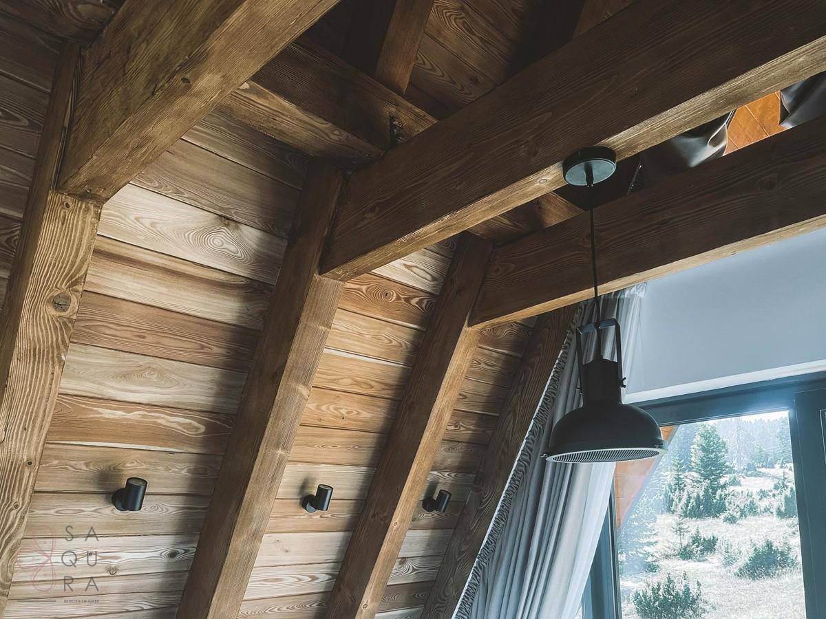 Rustikale Holzdecke mit sichtbaren Balken und moderner Beleuchtung in einem Schlafzimmer.