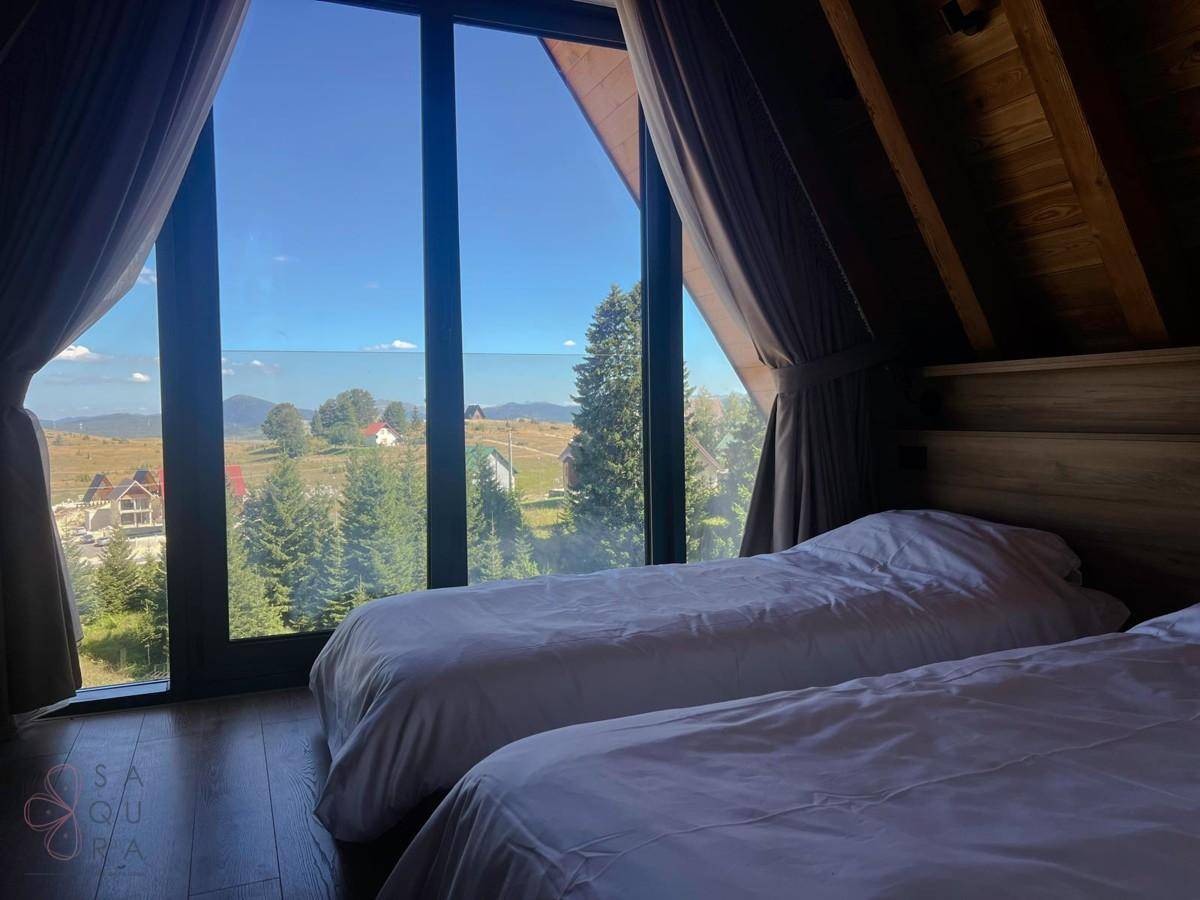 Helles Schlafzimmer mit zwei Einzelbetten und weitem Blick in die Natur durch große Fenster.